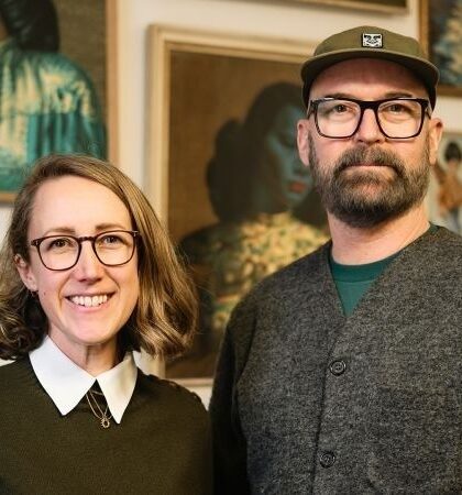 Två personer poserar framför konstverk i ett galleri eller en konstmiljö