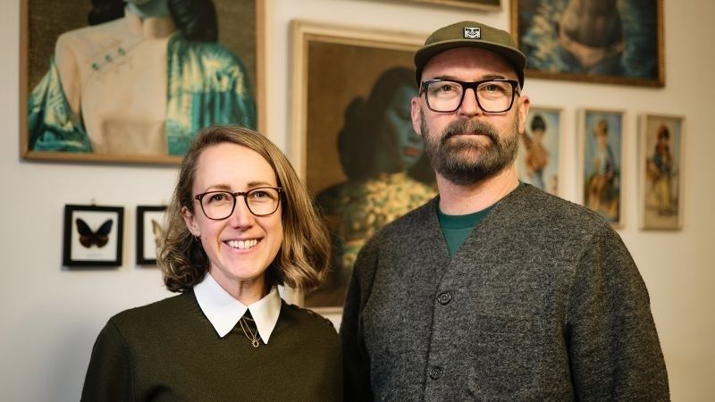 Två personer poserar framför konstverk i ett galleri eller en konstmiljö